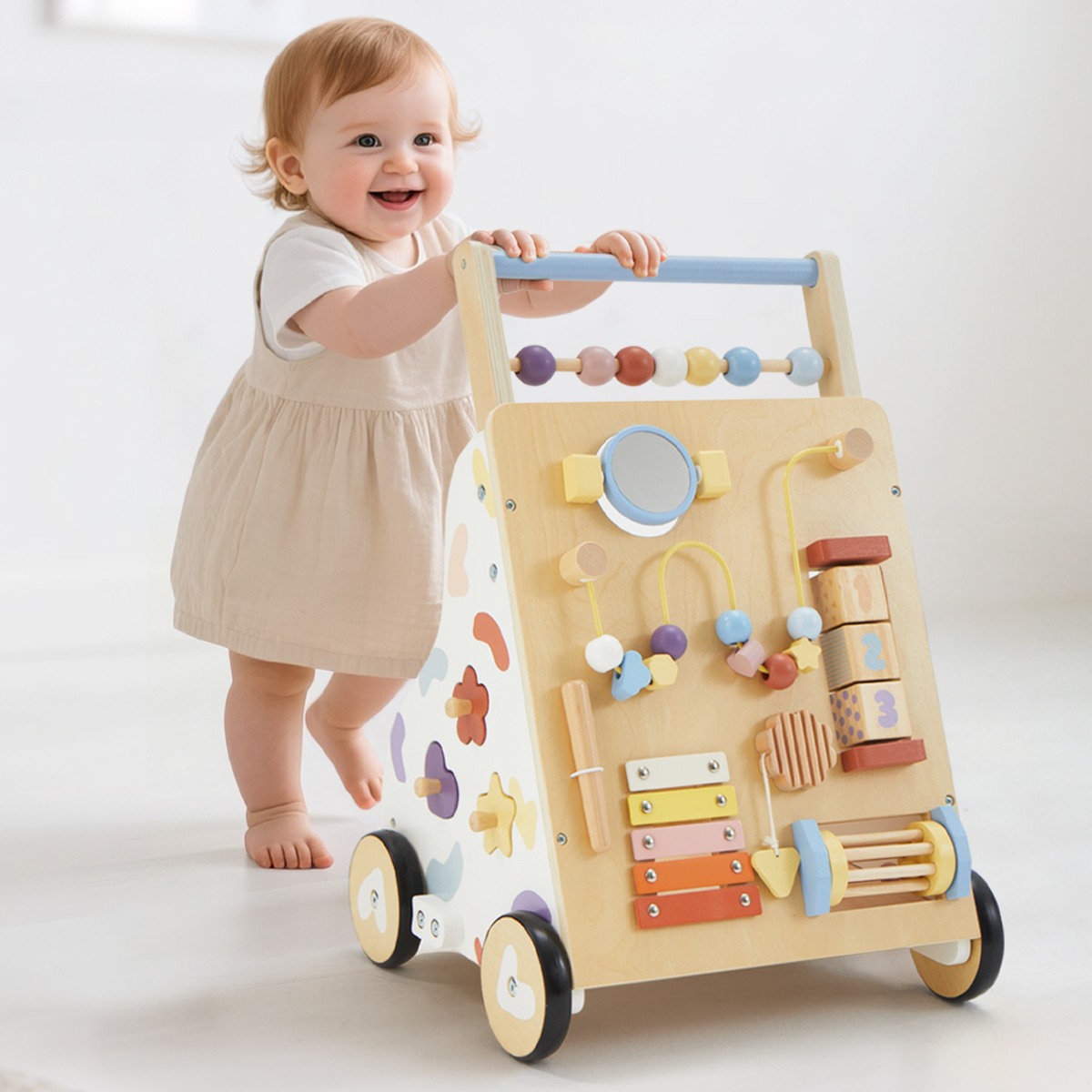 Smiling baby girl pushing pastel wooden montessori activity walker with xylophone