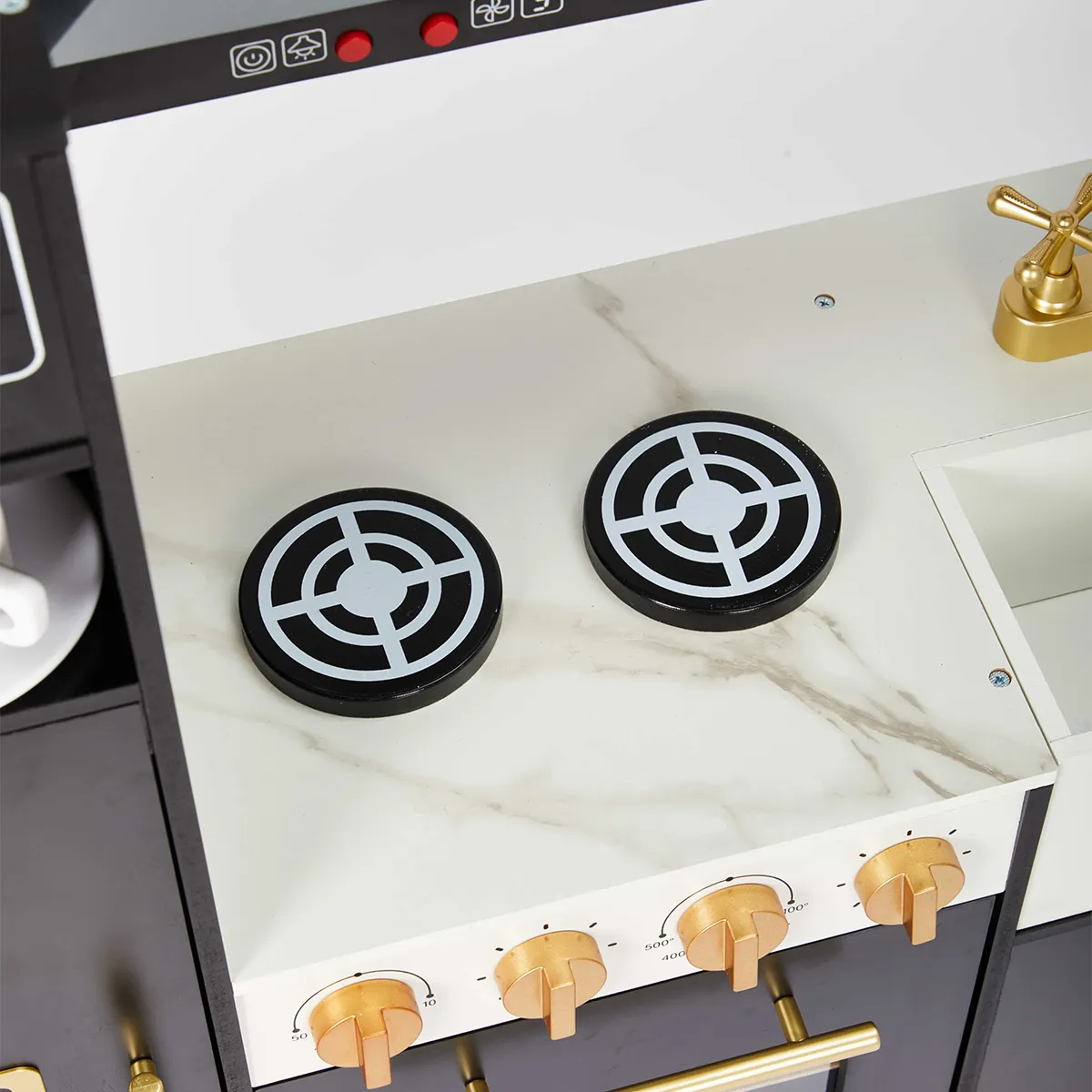 Close-up top view of marble pattern stovetop burners and gold knobs on wooden play kitchen